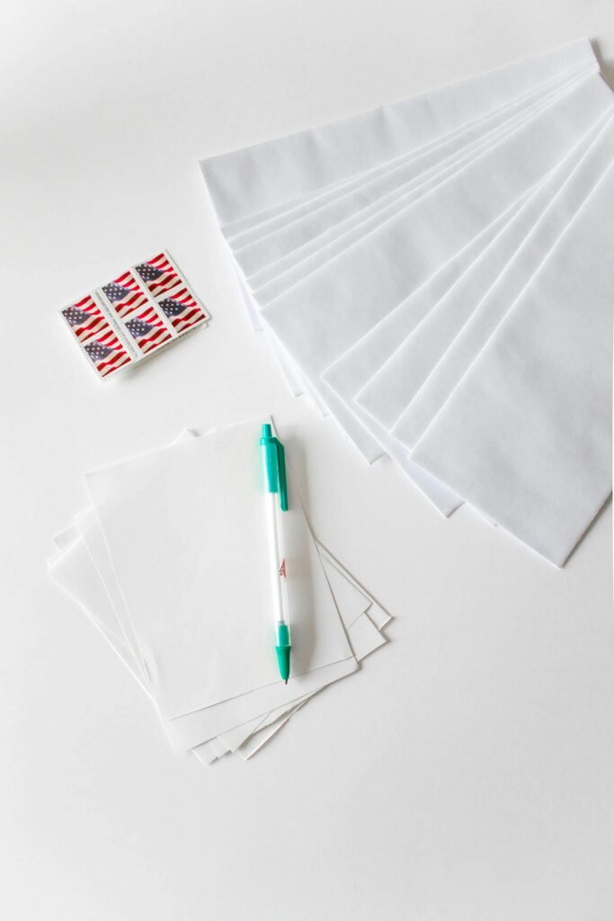 pexels-photo-1550341-1550341 Flat lay of envelopes, blank paper, pen, and American flag stamps on white background.